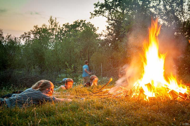 Jugendliche liegen im Gras und rösten an einem Stock Stockbrot über dem Feuer