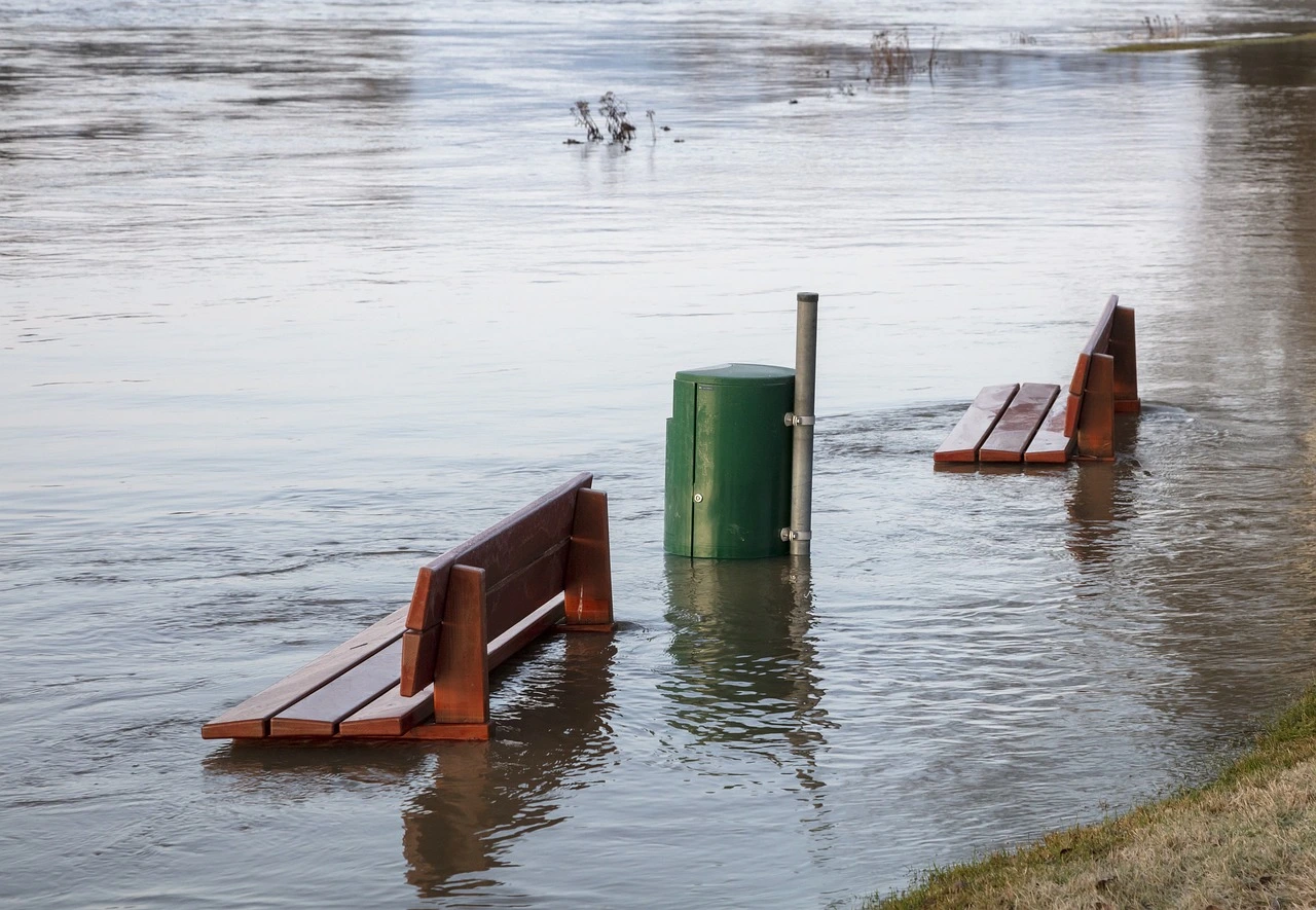 Das Foto zeigt eine Bank, die an einem überfluteten Flussufer steht.