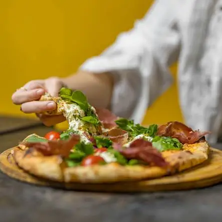Eine Person, die sich ein Stück Essen von einer Pizza schnappt