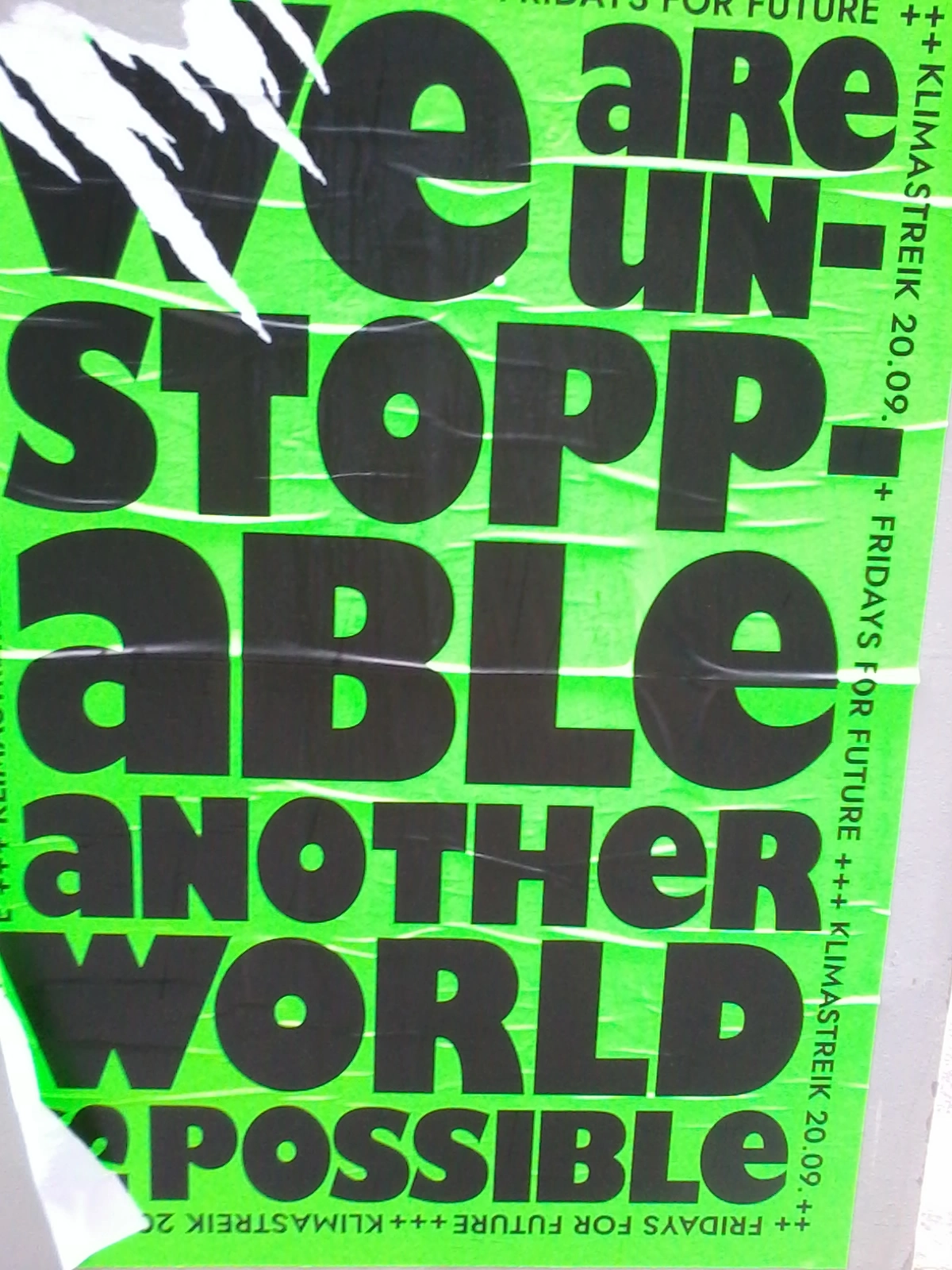 Das Foto zeigt ein grünes Plakat mit der Aufschrift "We are unstoppable, another world is possible!"
