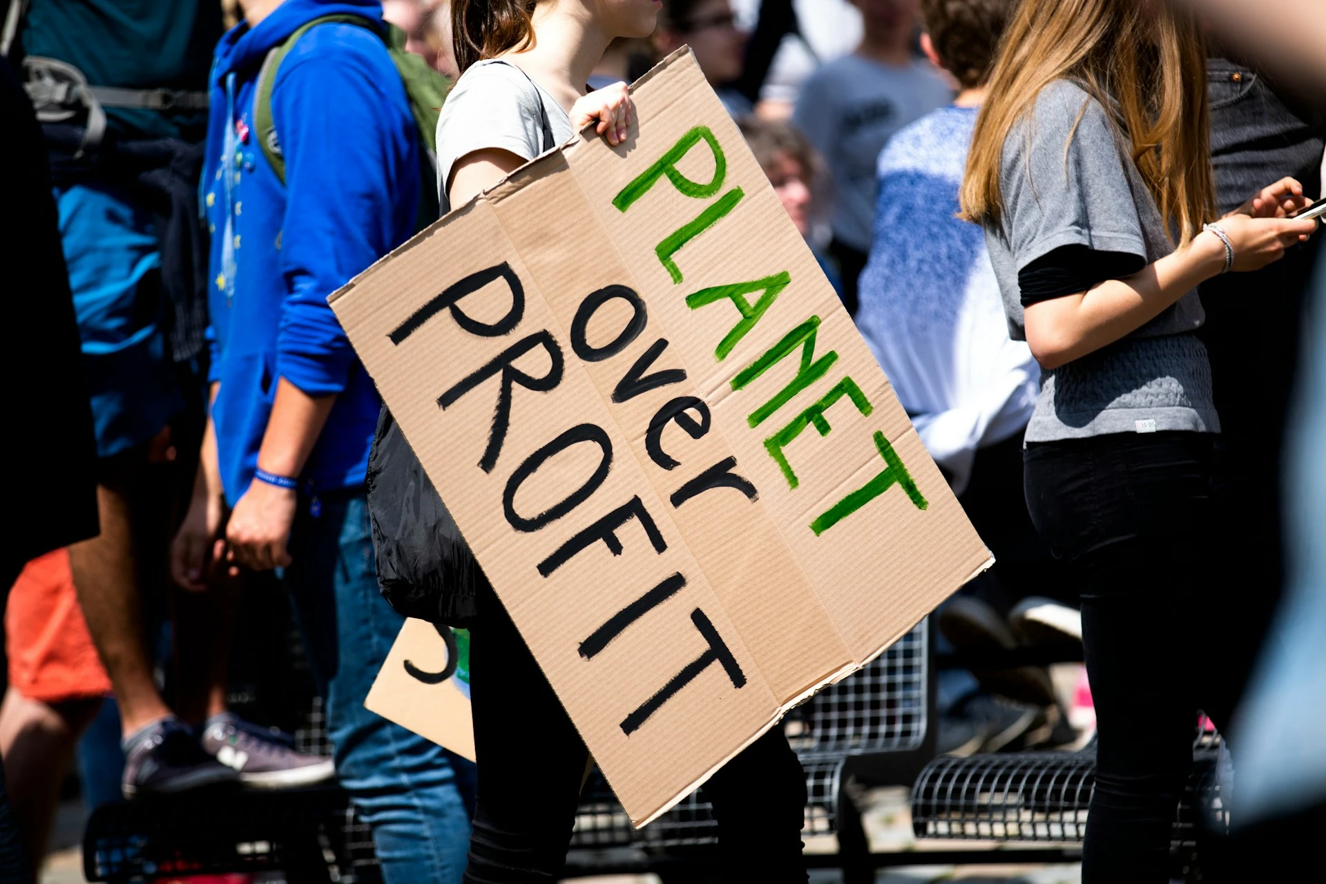 Das Foto zeigt eine demonstrierende Menschenmenge. Im Vordergrund ist ein Plakat mit der Aufschrift "Planet over profit" zu sehen.