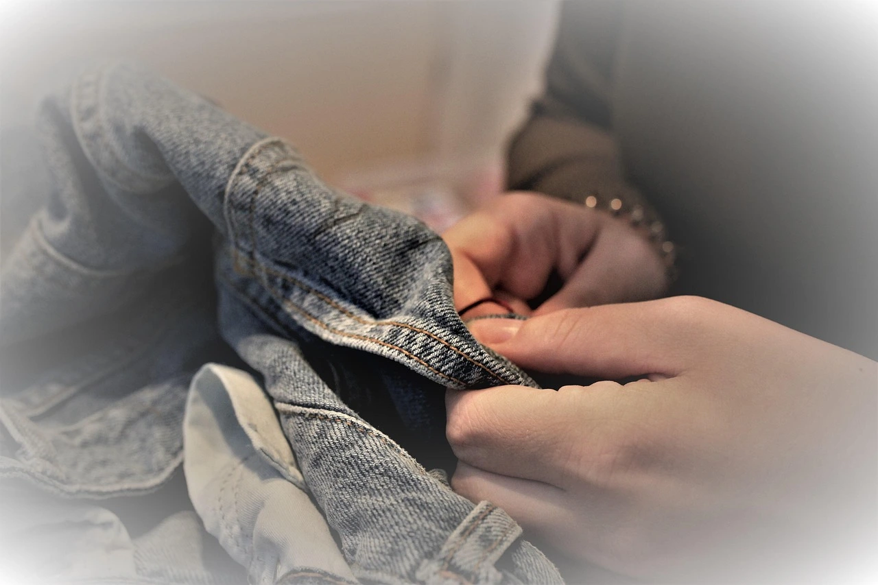 Das Foto zeigt eine Jeansjacke. Sie wird gerade von Hand geflickt.