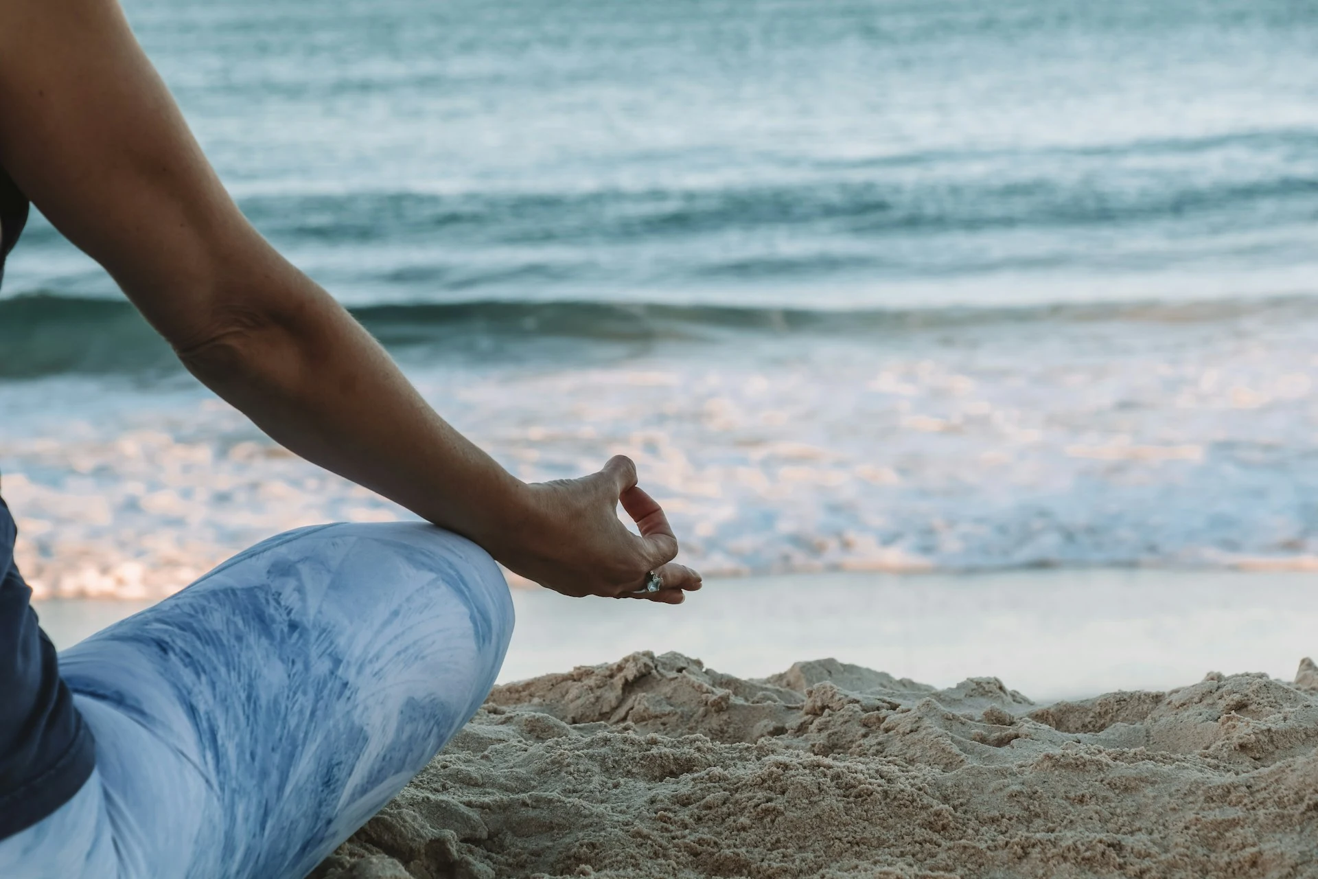 eine Person in Yoga-Haltung sitzt am Strand und blickt auf das Meer