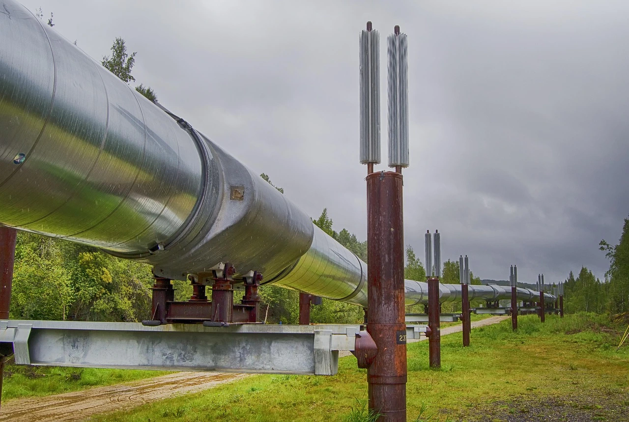 eine metallig-glänzende Pipeline auf Metallstreben führt durch Grasland