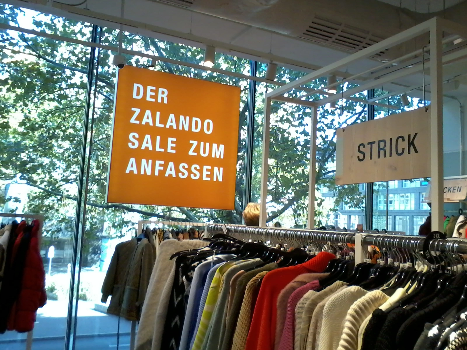 Das Foto zeigt ein Bekleidungsgeschäft von innen. Zu sehen ist eine lange Kleiderstange mit Strickwaren. Im Schaufestenster hängt ein "Zalando"-Schild.