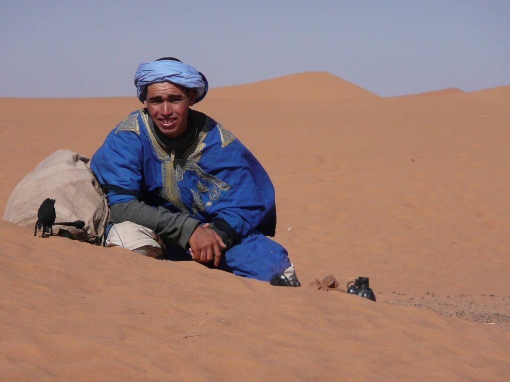 Ein Mann mit blauer Kleidung und blauem Turban sitzt in einer Sandwüste