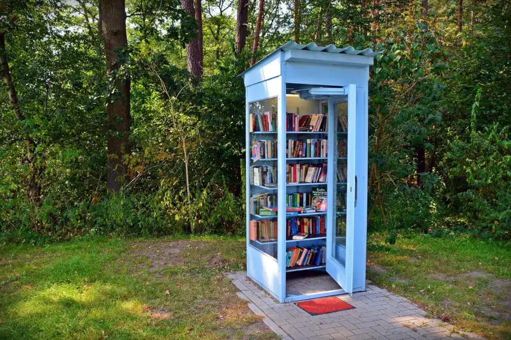 eine hellblaue Telefonzelle in einer Grünanlage, gefüllt mit Büchern