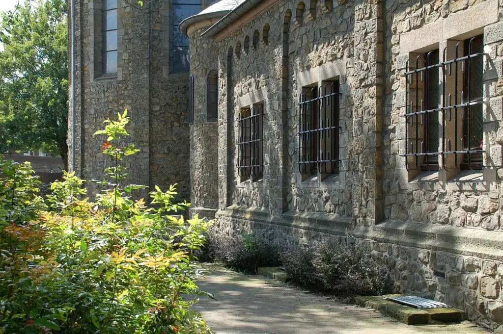 ein altes Gebäude mit Steinmauern und Gittern an den Fenstern, im Vordergrund Büsche