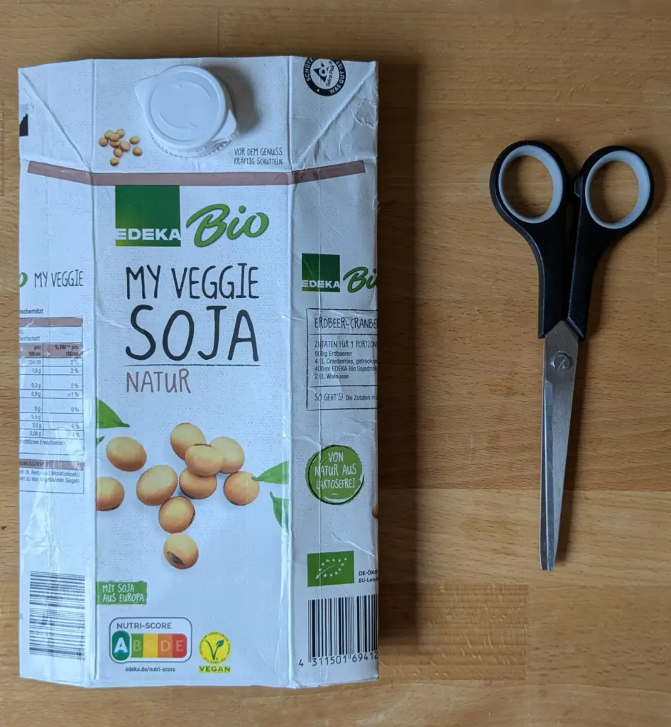 Ein BIld, das ein flachgedrücktes Tetrapak von einer Bio-Sojamilch zeigt. Rechts daneben befindet sich eine haushaltsübliche Schere.