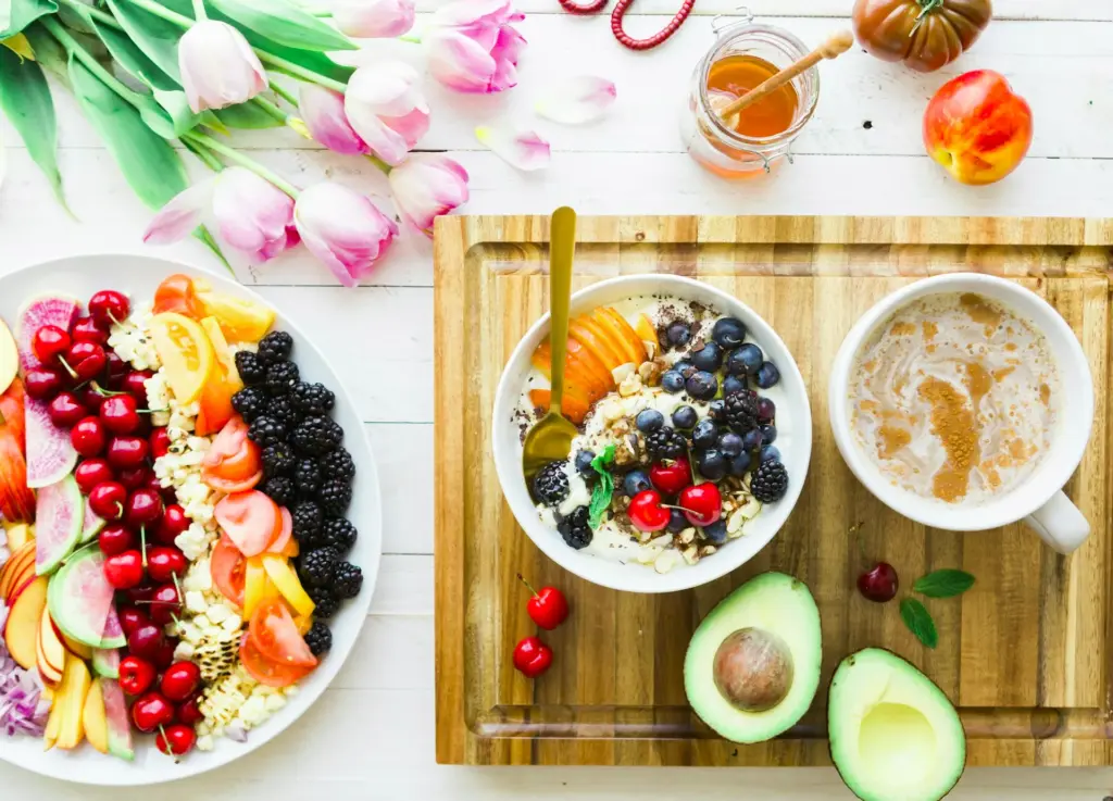ein reich gedeckter Tisch mit einer Schale Müsli mit Obst, Porridge, Tulpen und einer Bowl mit Obst