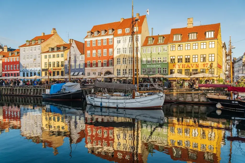 Blick in die Altstadt von Kopenhagen, im Vordergrund ein Flus mit Segelbooten am Kai, im Hintergrund bunte Häuser