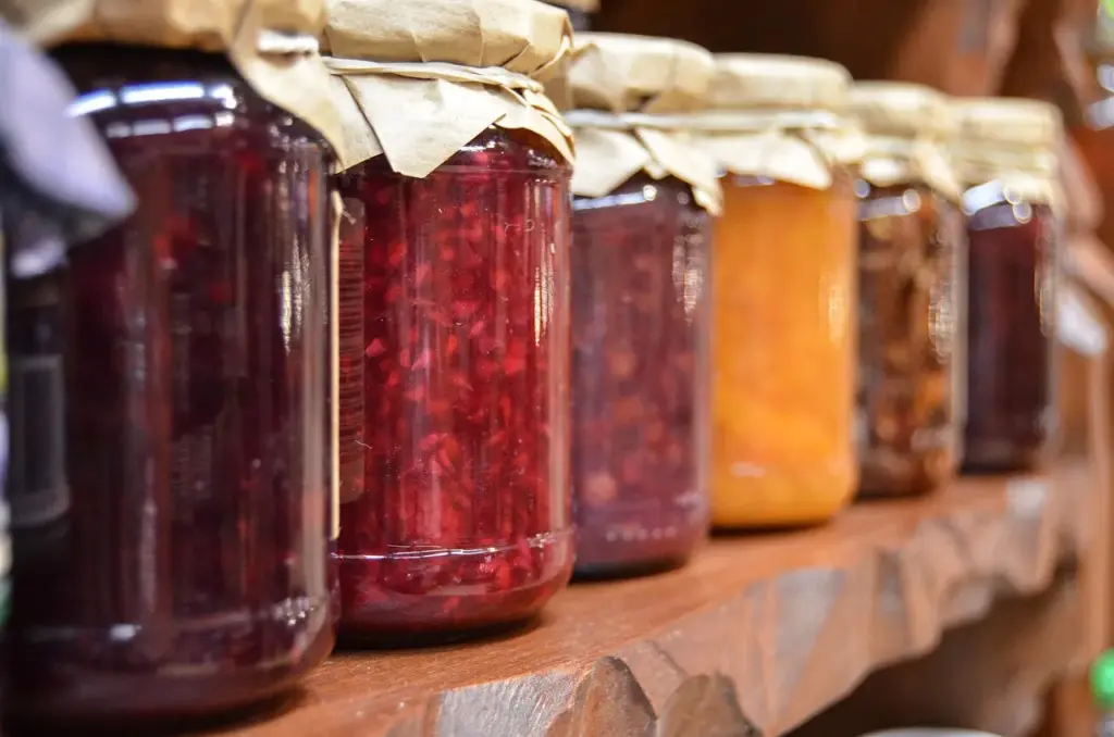 sechs Gläser mit verschiedenfarbiger Marmelade stehen nebeneinander auf einem Brett