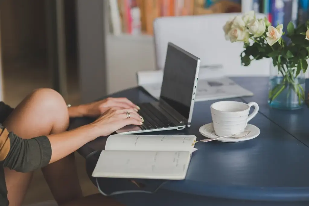 ein Laptop auf einem Tisch, daneben ein aufgeschlagenes Notizbuch und eine Kaffeetasse.