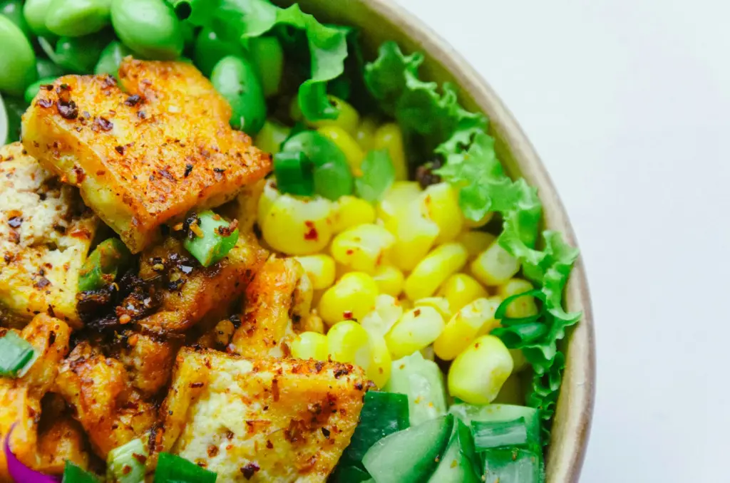 eine Schale mit grünem Salat, Mais und gebratenem Tofu