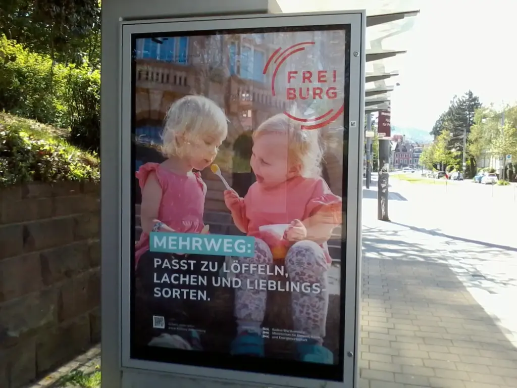 Zwei Plakate an Straßenbahnhaltestellen mit der Aufschrift "Mehrweg passt zu Pizza, Pasta und zum ersten Date" bzw. "Mehrweg passt zu Löffeln, Lachen und Lieblingssorten"