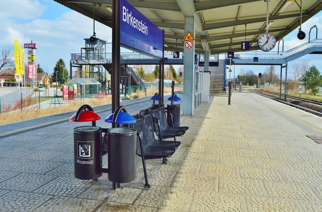 Blick auf einen Bahnhof, zwischen zwei Gleisen befinden sich Müllbehälter und SItzgelenheiten.